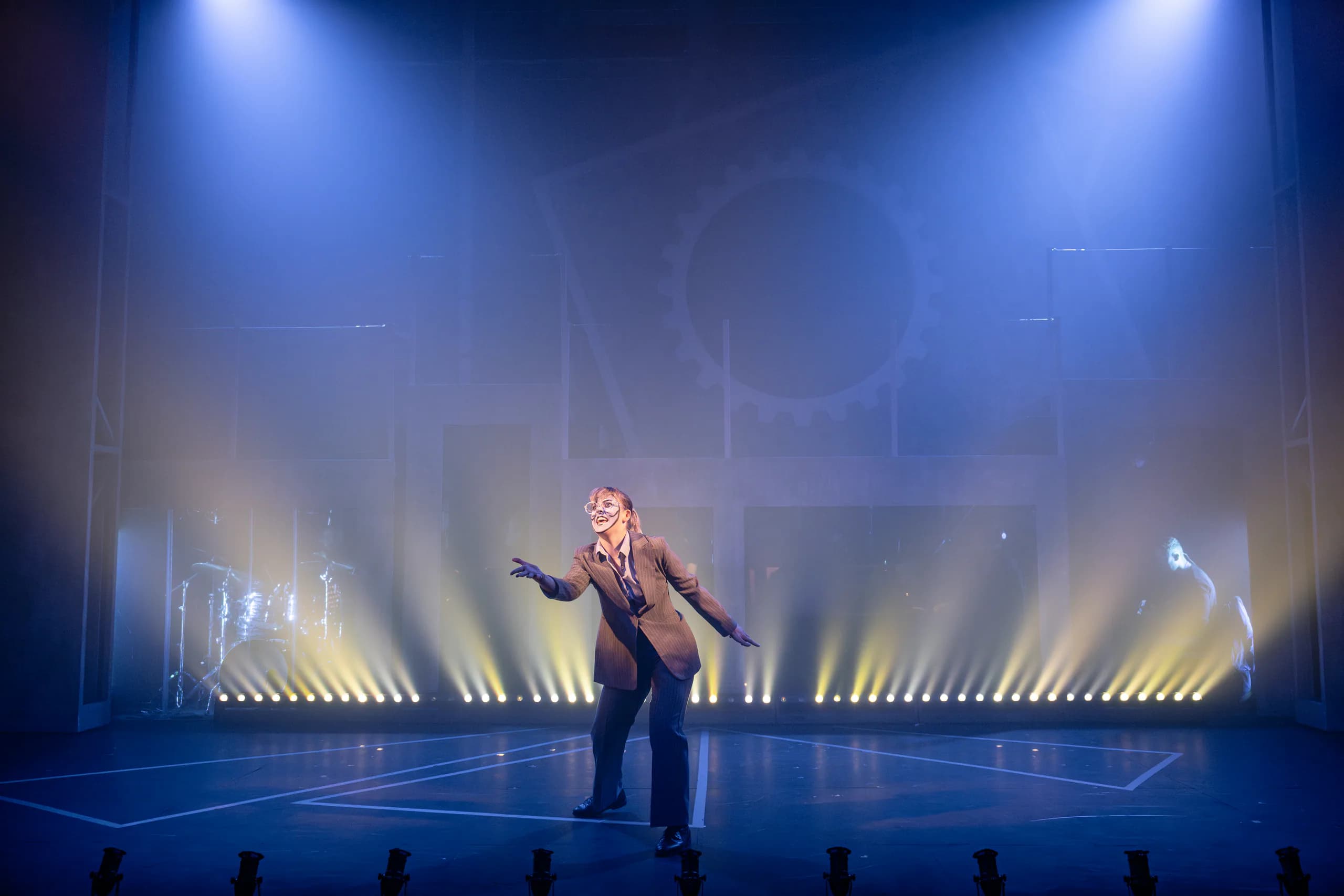 9 to 5 at Mountview: solo performer in a suit mid-song, centre stage, with blue haze and a row of warm backlights